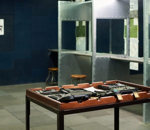 Firearms displayed in middle of a shooting range featuring individual booths. Posters on wall and stool in the background add context to shooting environment